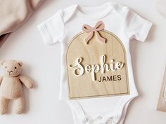 a baby's bodysuit and teddy bear on a white table with other items