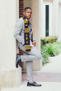 a man wearing a suit and tie leaning against a pillar