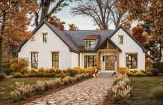 a white house surrounded by trees and bushes with a stone path leading to the front door