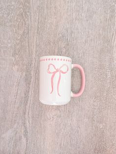 a pink and white coffee mug with a bow on it sitting on a wooden surface