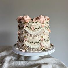 a three tiered cake with pink flowers and pearls on the top is sitting on a white plate