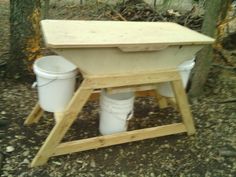 two buckets sitting on top of a wooden stand in the woods next to trees