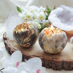 three candles are sitting on a piece of wood with flowers in the background and white orchids