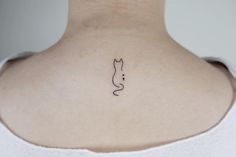 the back of a woman's neck with a small cat tattoo on her left shoulder