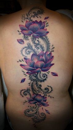 the back of a woman's body with tattoos on it and flowers in the middle