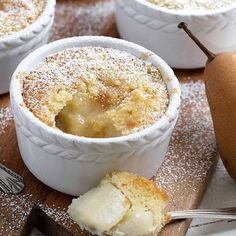 small white bowls filled with dessert sitting on top of a wooden cutting board next to a pear