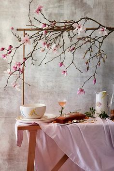 a table topped with a bowl and plate next to a vase filled with pink flowers