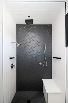 a walk in shower sitting next to a white bench and black tiled wall behind it