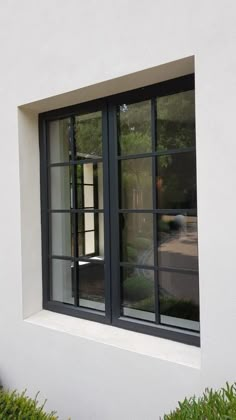 an open window on the side of a white building with green bushes in front of it