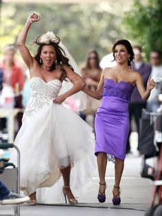 two women in dresses are walking down the street with their arms up and one is holding her hand out