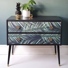 a black and gold painted dresser next to a pineapple plant on top of it