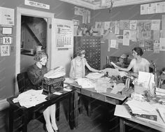 three women sitting at a desk with papers and other items on top of the table