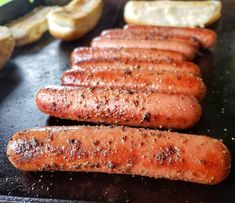 several sausages are being cooked on a grill with lemon wedges and bread slices