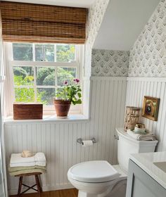 a white toilet sitting next to a window in a bathroom under a wooden flooring