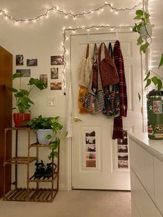 a white door with some plants and pictures on the wall next to it that has lights strung above