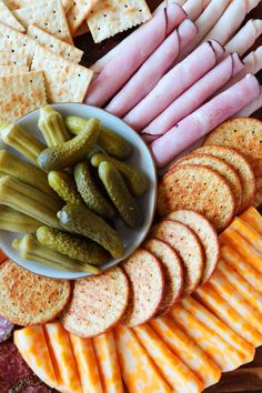 an assortment of cheeses, crackers and pickles on a platter with meat