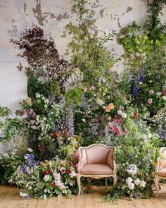 two chairs sitting next to each other in front of a wall with flowers and plants