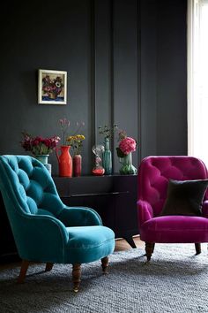 two colorful chairs in front of a black wall with vases and flowers on it