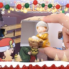 a hand is holding a small figurine in front of a christmas scene