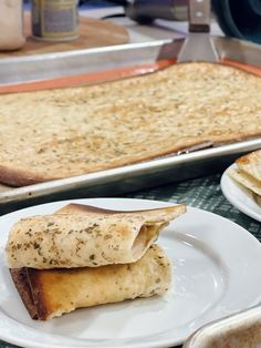 two white plates with food on them next to a baking pan filled with flat bread