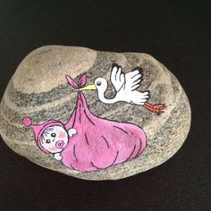 a painted rock with a stork carrying a baby girl on it's back