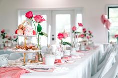 a white table topped with lots of pink flowers and candles next to plates filled with food