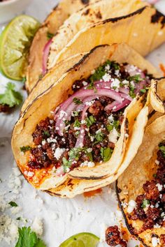 three tacos with meat, onions and cilantro on paper next to lime wedges