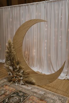 a large wooden moon sitting on top of a rug next to a christmas tree in front of a curtain