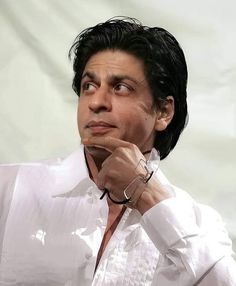 a close up of a person wearing a white shirt and black bracelet with his hand on his chin