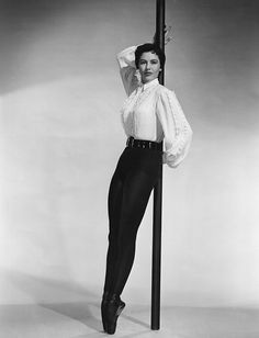 an old photo of a woman leaning on a pole