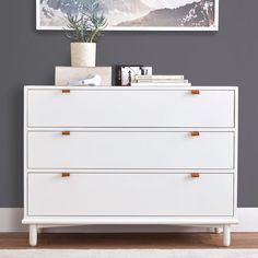 a white dresser sitting in front of a wall with a painting on top of it