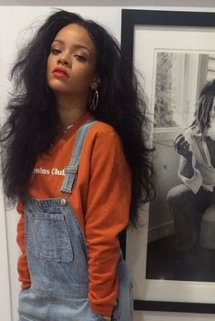 a woman with long black hair wearing an orange shirt and overalls standing in front of a mirror