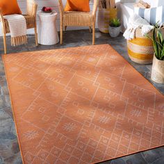 an orange rug on the ground in front of some chairs and potted plants,