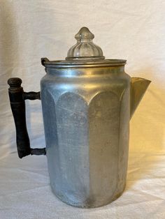 an old metal coffee pot with a lid and handle on a white cloth covered background