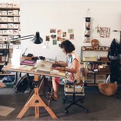 a woman sitting at a desk working on a piece of paper in an art studio