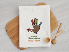 a white dish towel with a thanksgiving turkey on it next to two wooden spoons