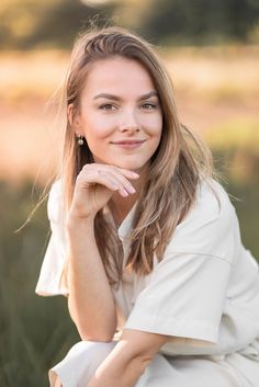 a woman sitting in the grass with her hand on her chin and looking at the camera