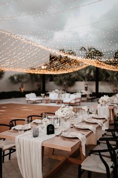 tables set up for an event with white linens and lights strung above the tables