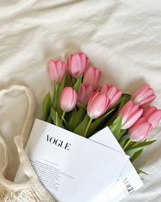 a bouquet of pink tulips sitting on top of a bed next to an envelope