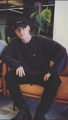 a young man sitting on top of a couch next to a plant in a living room