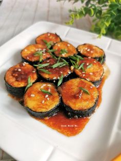 a white plate topped with sushi covered in sauce and garnished with green leaves