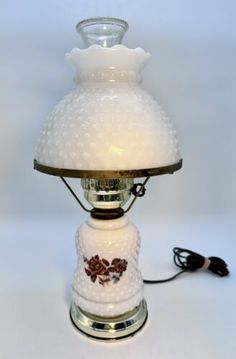 a white lamp with a glass shade on it's top and cord attached to the base