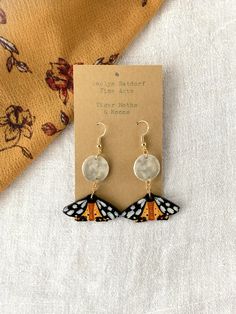 Title: Tiger Moths & Moons Looking for a unique handmade addition to your jewelry box? This pair of lovingly hand-painted wooden earrings will add artistic flair to your wardrobe or a personal touch to your gift to a loved one.  These original handcrafted earrings are hand painted on balsa wood with sterling silver hooks for sensitive ears (the gold hooks are gold plated sterling silver). Each pair of earrings in my shop is carved and painted by hand, and the item you receive is the exact one seen in the photos. The earrings are lightweight and hypoallergenic. This gift can be personalized with a special note and sent directly to friend or loved one. Please add the note during checkout using the box Etsy provides for "Notes to Seller." Looking for a different design? Check out my shop to f Hand Painted Earrings Wood, Artsy Earrings, Wooden Butterfly, Gold Hooks, Body Accessories, Balsa Wood, Hand Painted Earrings, Types Of Earrings, Polymer Clay Jewelry Diy