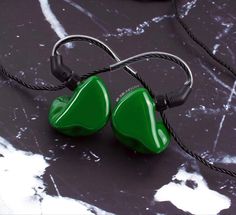 two green heart shaped earbuds sitting on top of a black table next to wires