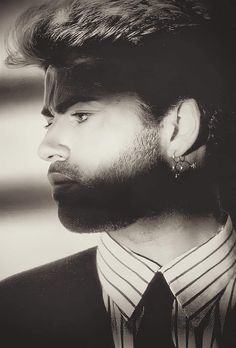 a black and white photo of a man wearing a suit with his hair pulled back