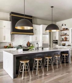 a large kitchen with white cabinets and black counter tops, gold pendant lights over the island