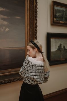 a woman standing in front of a painting wearing a black and white top with an off the shoulder neckline