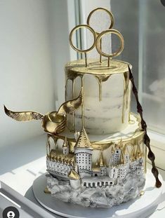 a three tiered cake with gold and white decorations on the top is sitting in front of a window