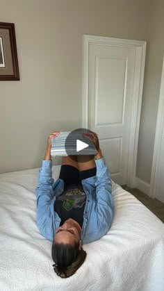 a woman laying on top of a bed holding a laptop computer over her head and looking at the camera