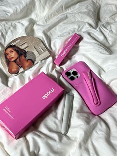 a pink cell phone sitting on top of a bed next to a magazine and pen